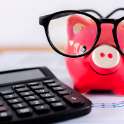 Calculator on paper with piggy bank in background.
