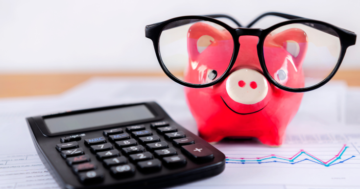 Calculator on paper with piggy bank in background.